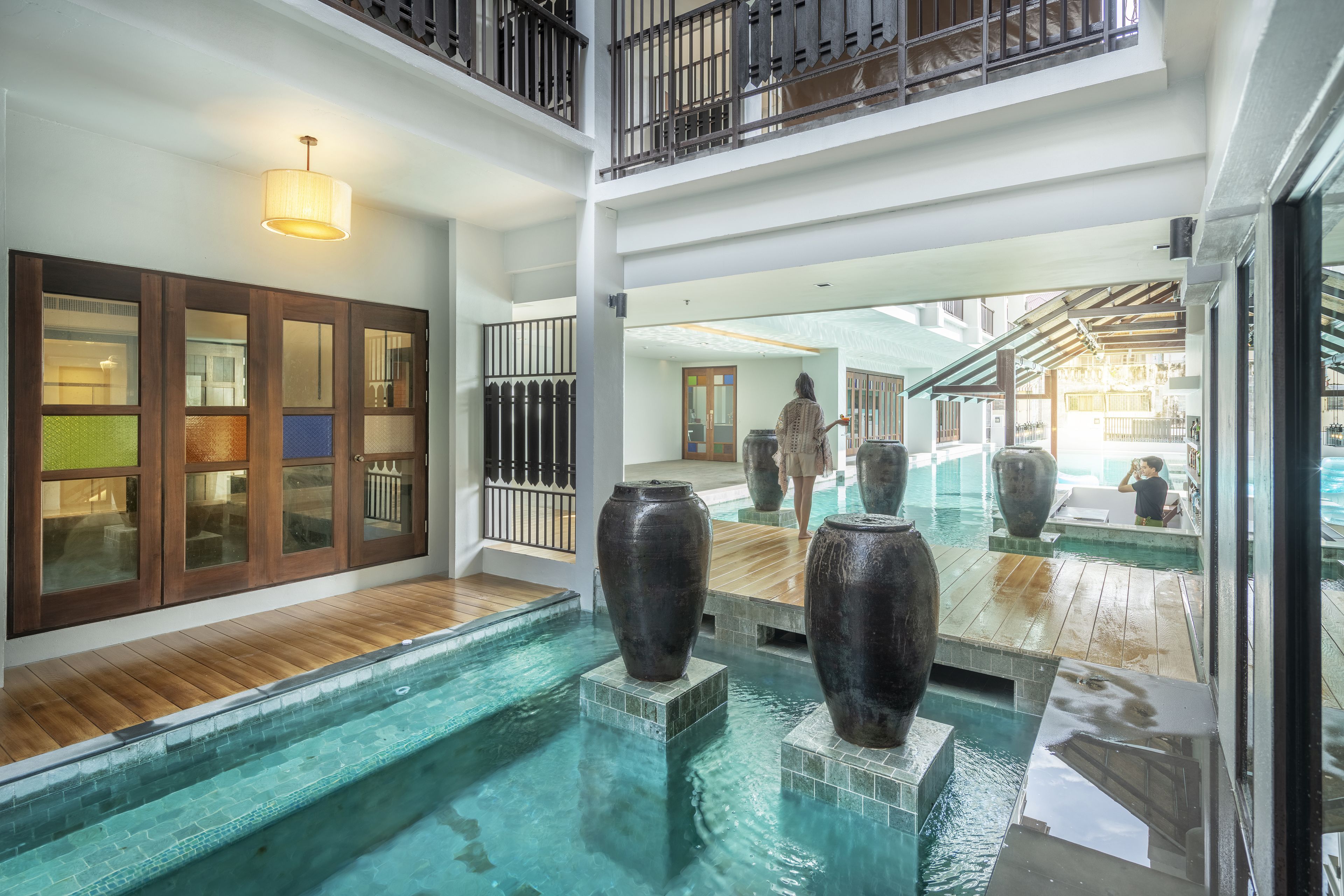A multi-level indoor pool area with wooden flooring, large vases, and a glass railing.