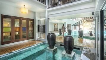 A multi-level indoor pool area with wooden flooring, large vases, and a glass railing.