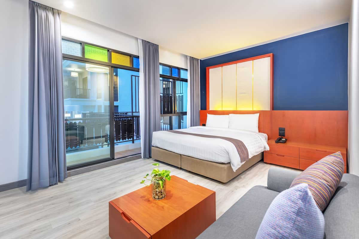 Quarto de hotel moderno com uma cama grande, um sofá, uma mesa de centro de madeira com uma planta e vista para a cidade através de amplas janelas.