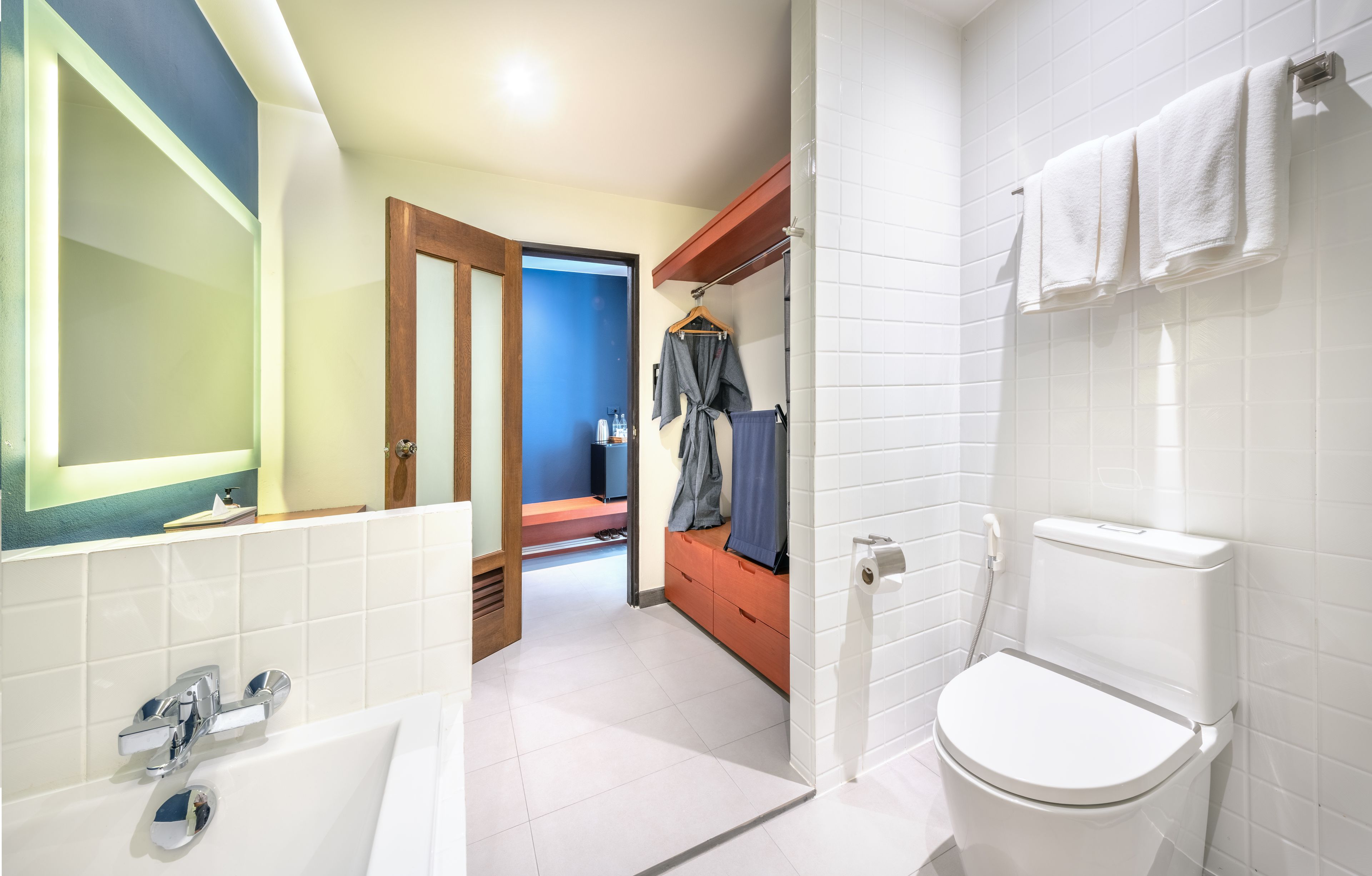 Un baño moderno con un inodoro blanco, un lavabo con grifo cromado y un espejo con marco iluminado.