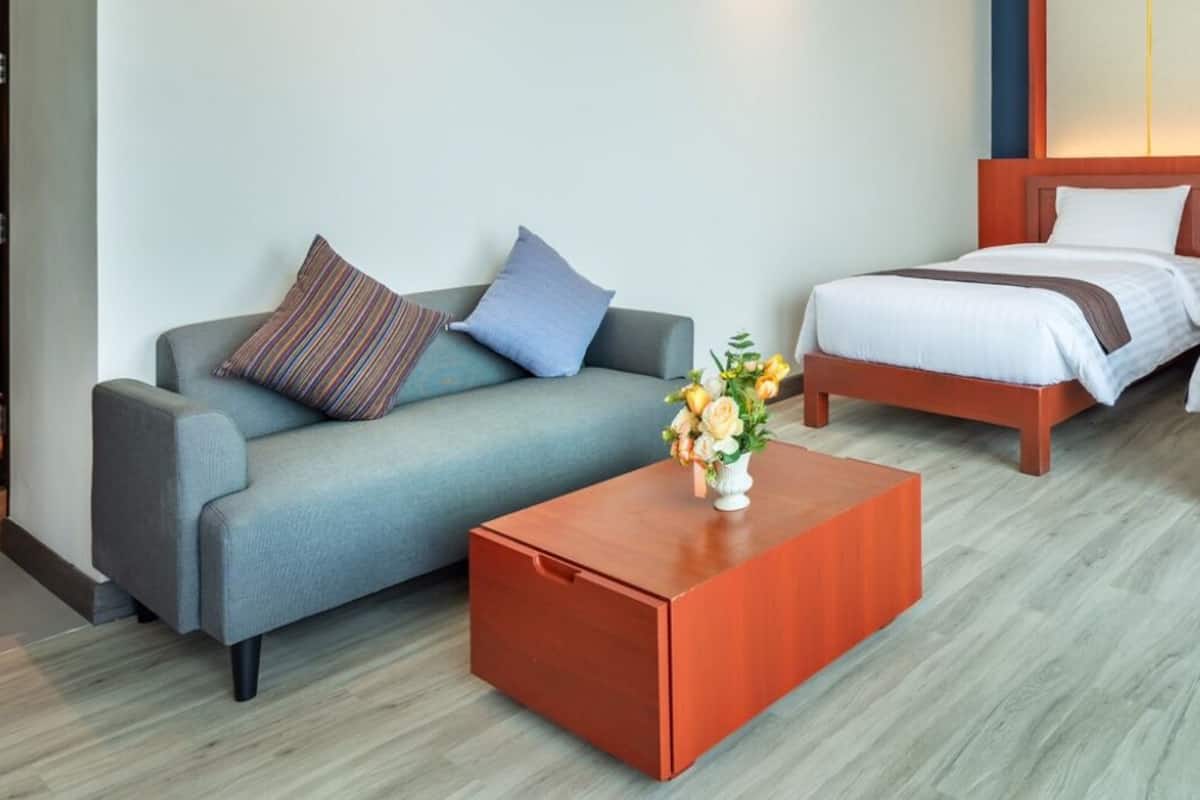Quarto de hotel com sofá cinzento, duas camas de solteiro e uma mesa de centro de madeira.