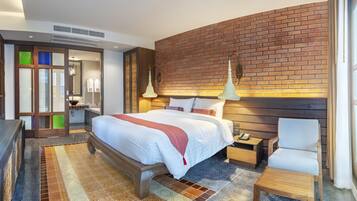 Una habitación de hotel moderna con una cama grande, una mesita de noche de madera, una silla, un baño con espejo y lavabo, y una pared de ladrillo decorativa.