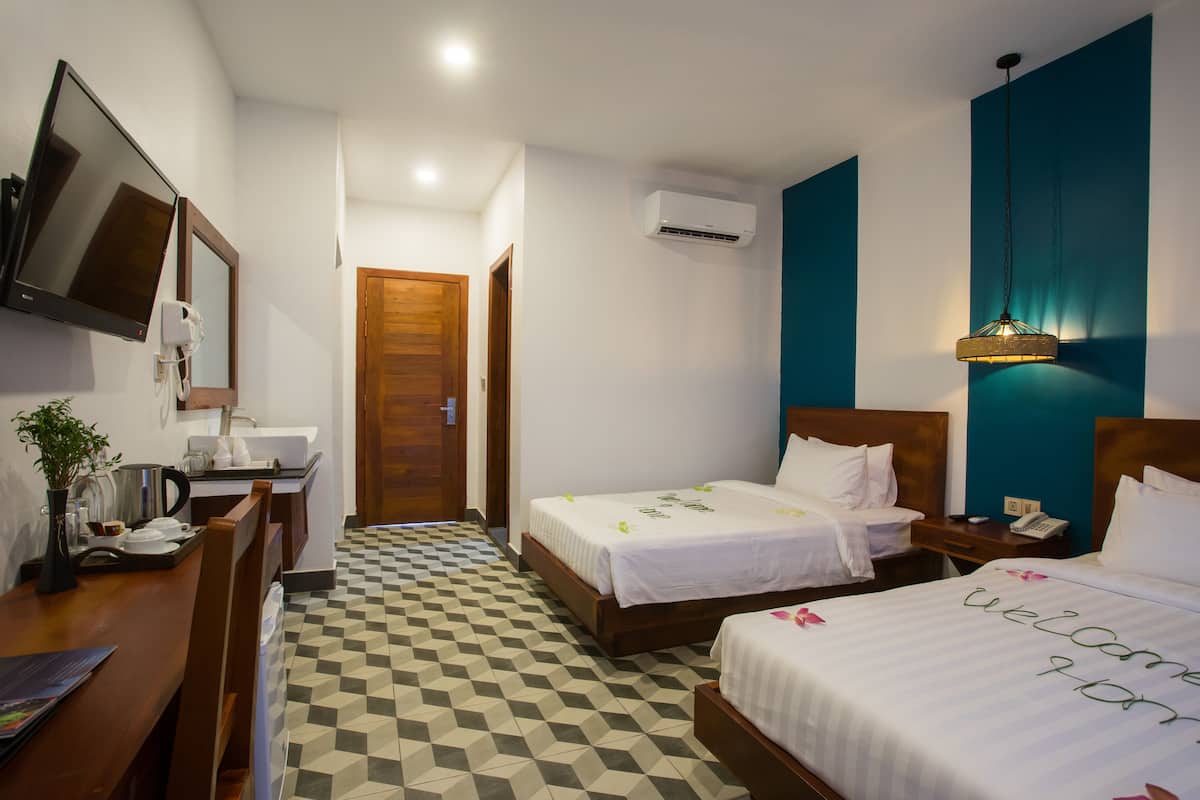 Een hotelkamer met twee bedden, een bureau met een computer, een televisie en een airconditioner.