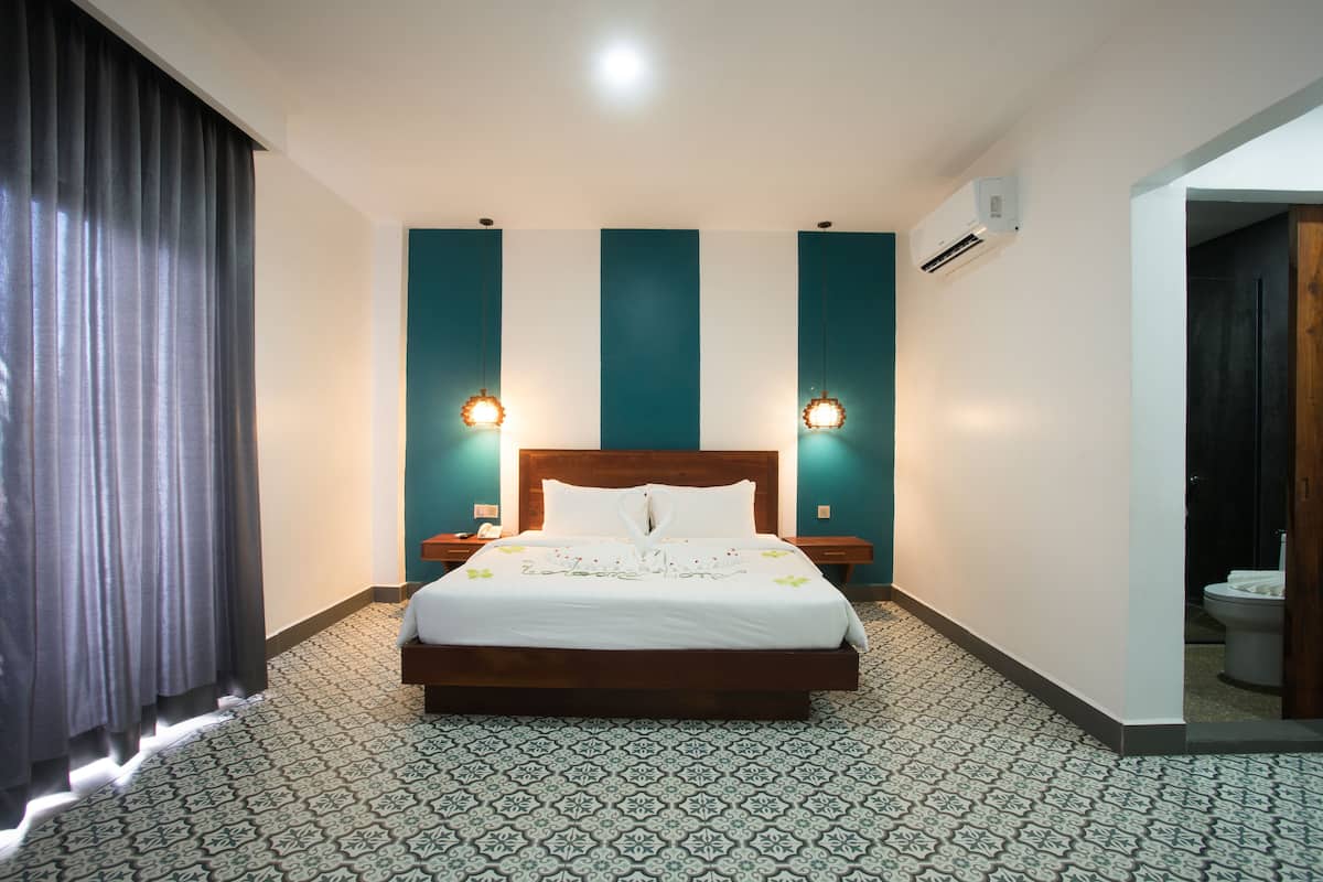 Een hotelkamer met een groot bed, een nachtkastje, een wandairconditioner en een kamer met een patroon vloer.