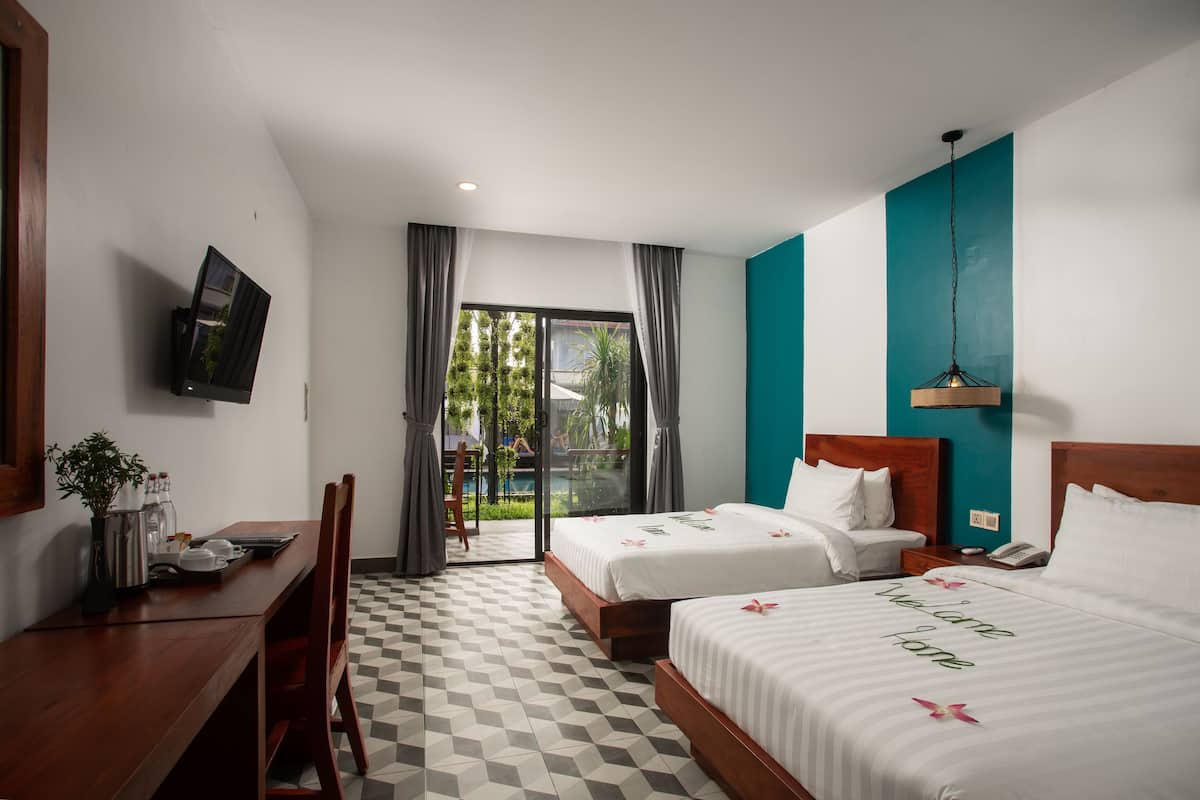Een hotelkamer met twee bedden, een bureau, een televisie en uitzicht op een zwembad en groen.