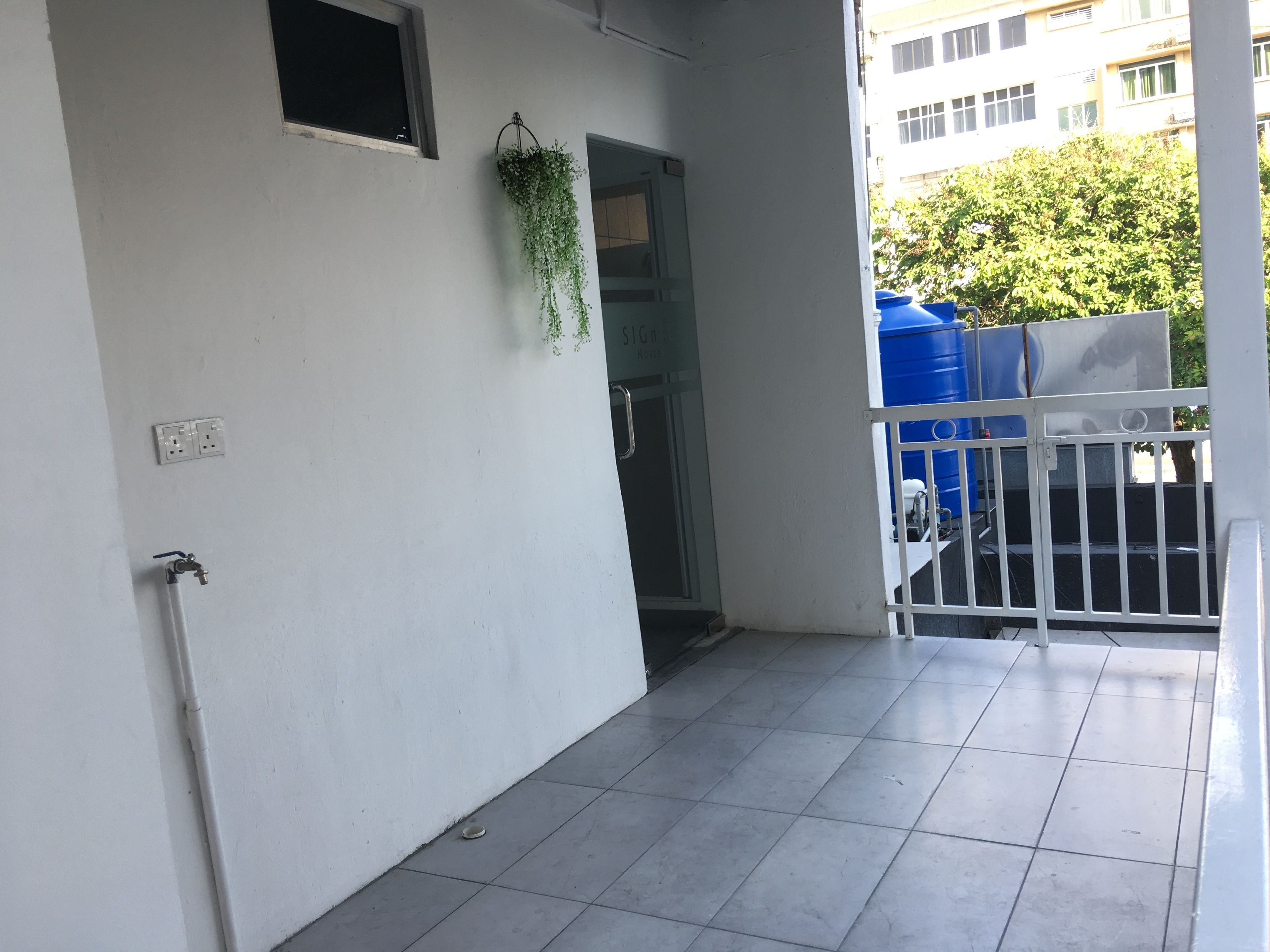 A balcony with a white railing, a potted plant, and a view of a building with a window and a door.