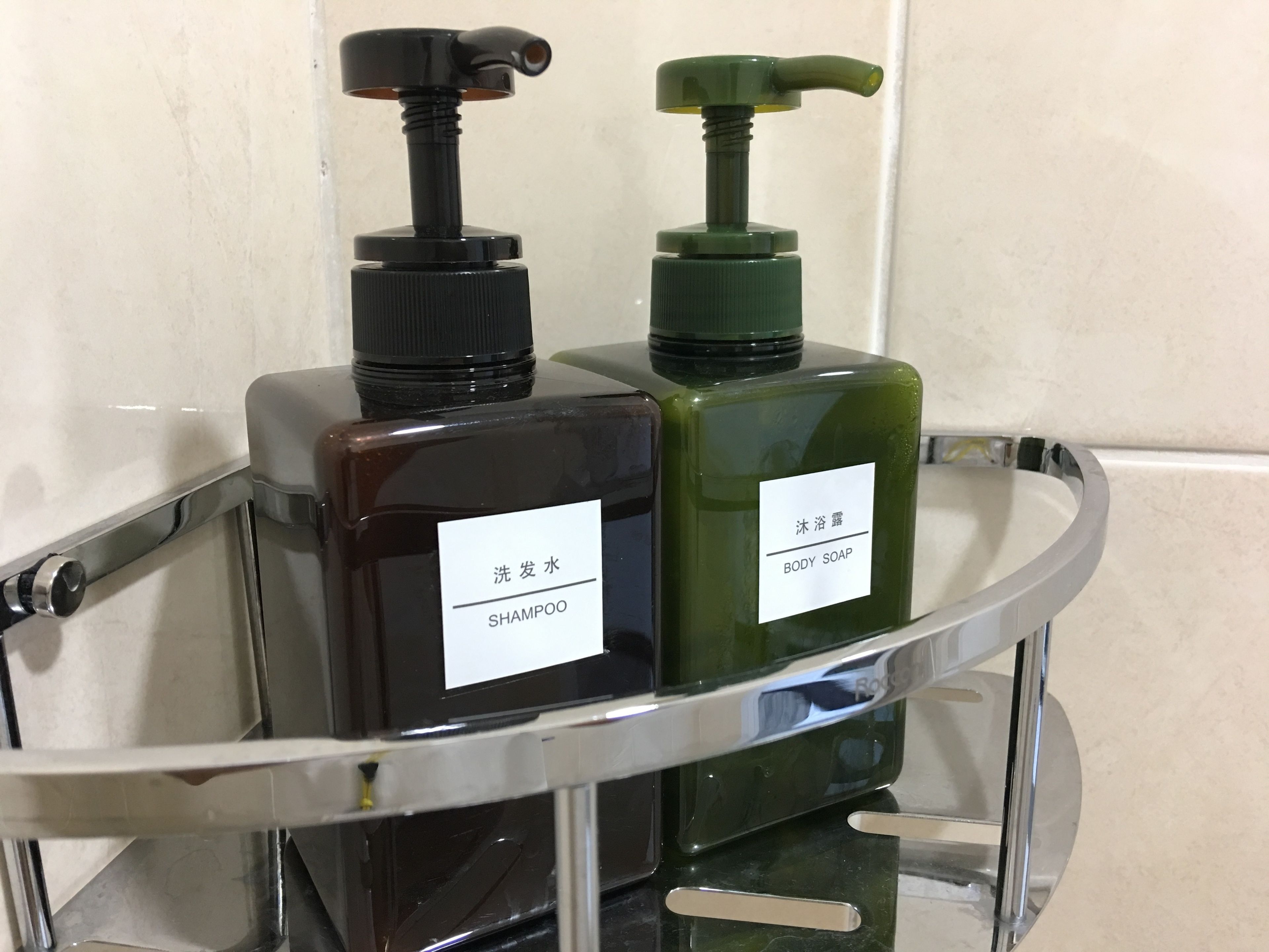 To flasker shampoo og badesæbe på en hylde i et badeværelse.