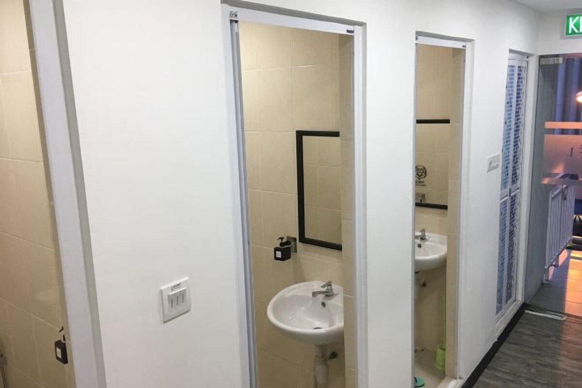 A corridor with a white wall, a door leading to a bathroom with a sink and mirror, and a tiled floor.