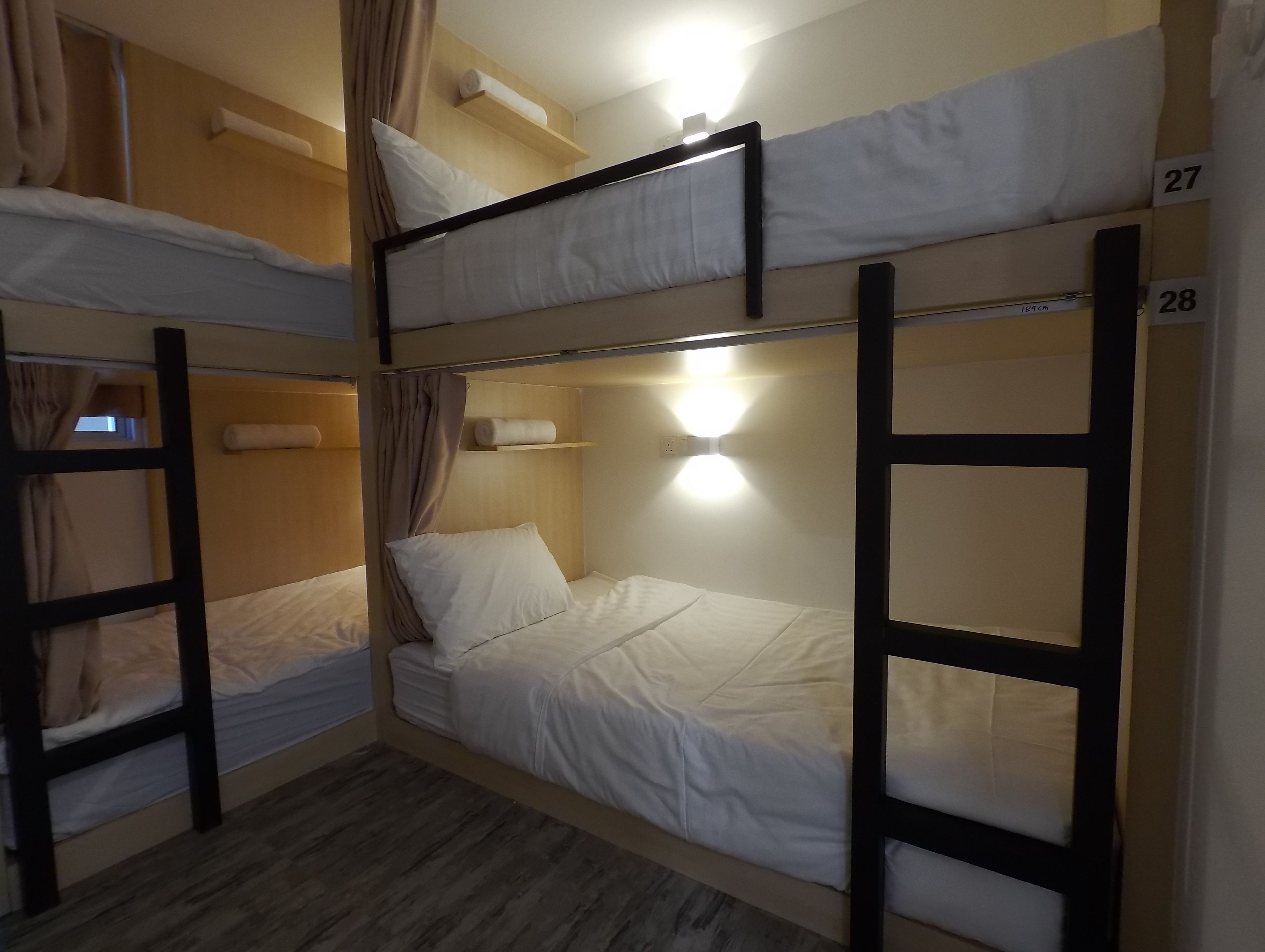 A bunk bed room with three levels, each with a pillow and a rolled towel. There is a wall-mounted light fixture above the middle bunk.