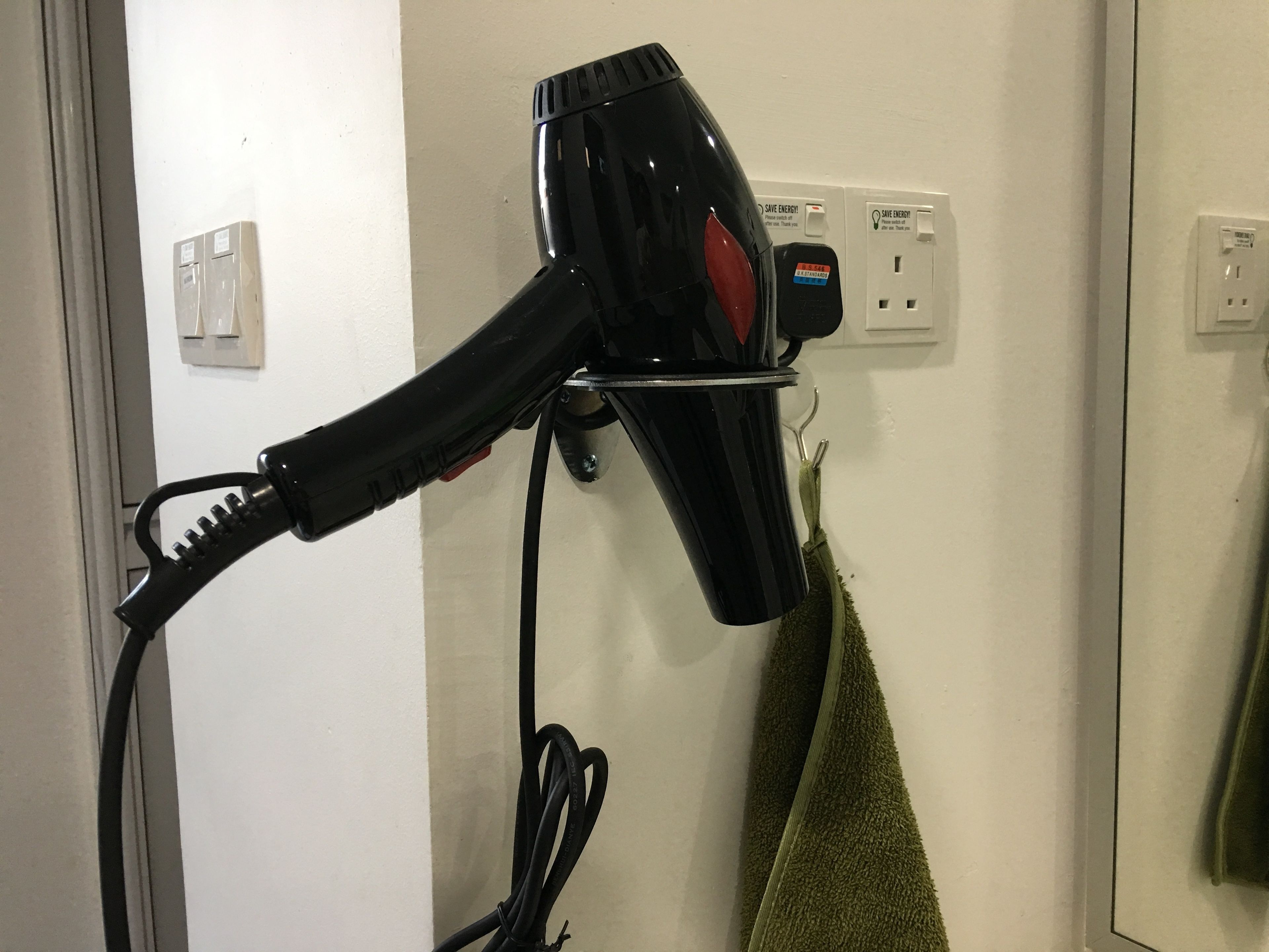 A hair dryer mounted on a wall with a power outlet nearby.