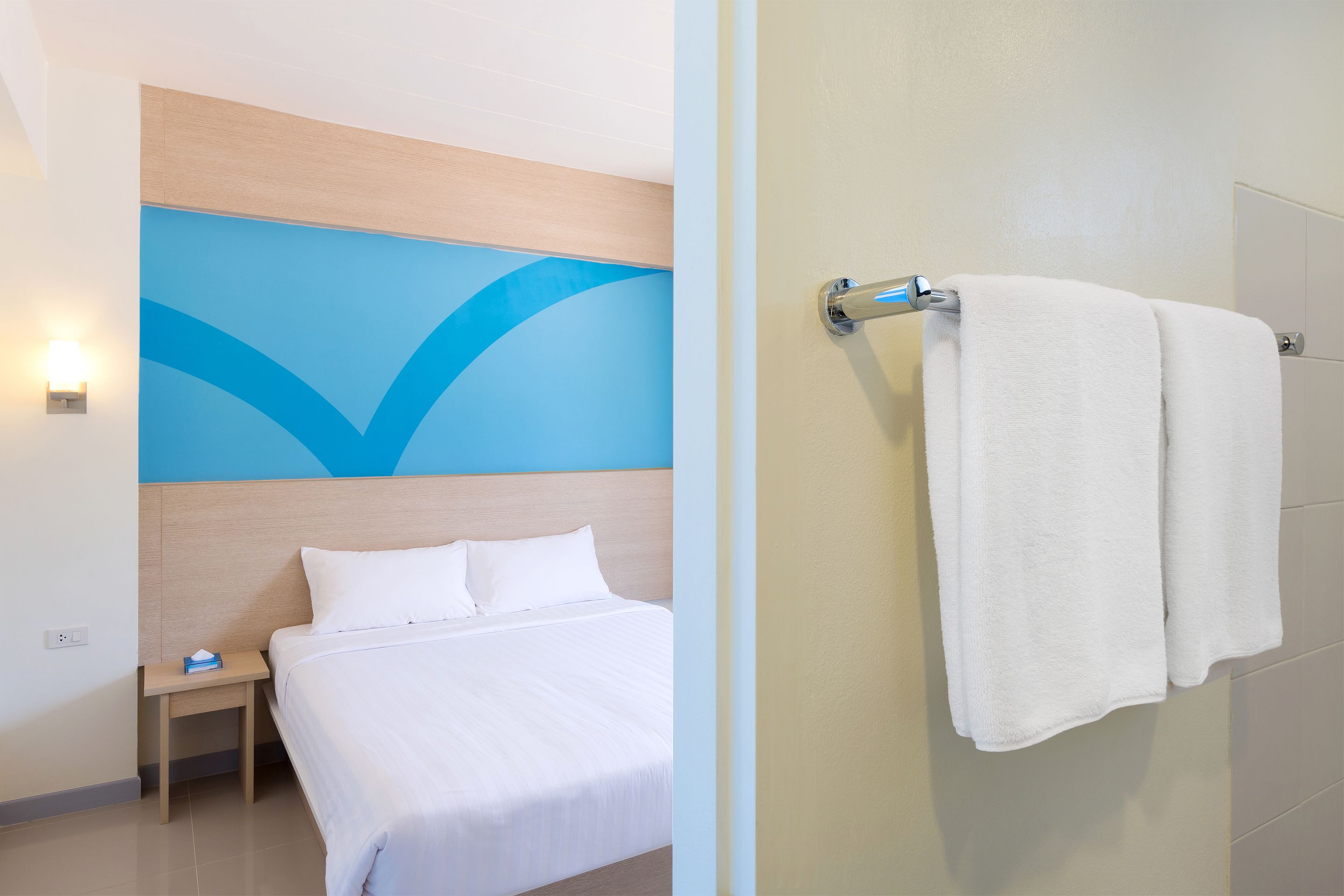 A hotel room with a bed, a nightstand, a wall with a blue design, and a towel rack with a towel.