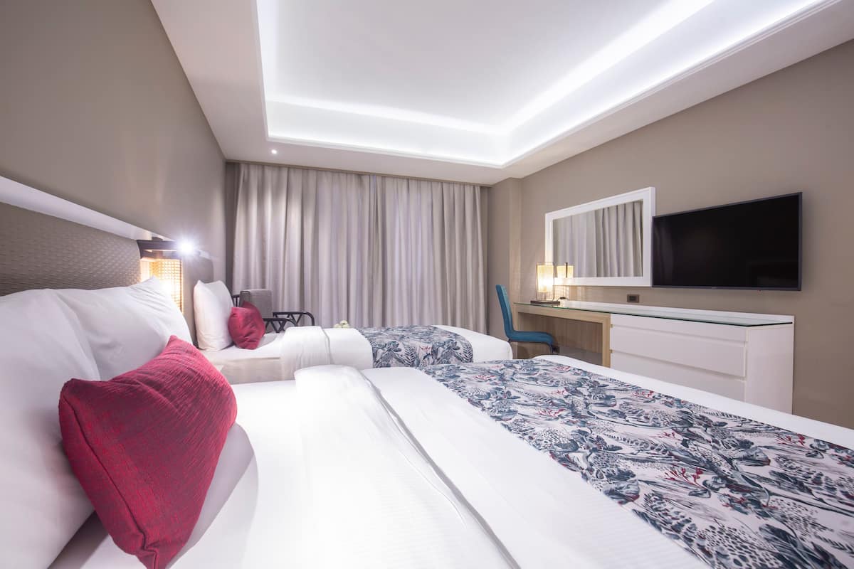 Une chambre d’hôtel avec deux lits, un bureau, une chaise, une télévision et une grande fenêtre avec des rideaux.