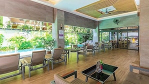 Un vaste espace intérieur aménagé avec des coins salon, offrant une vue sur la piscine et comprenant un restaurant en arrière-plan.