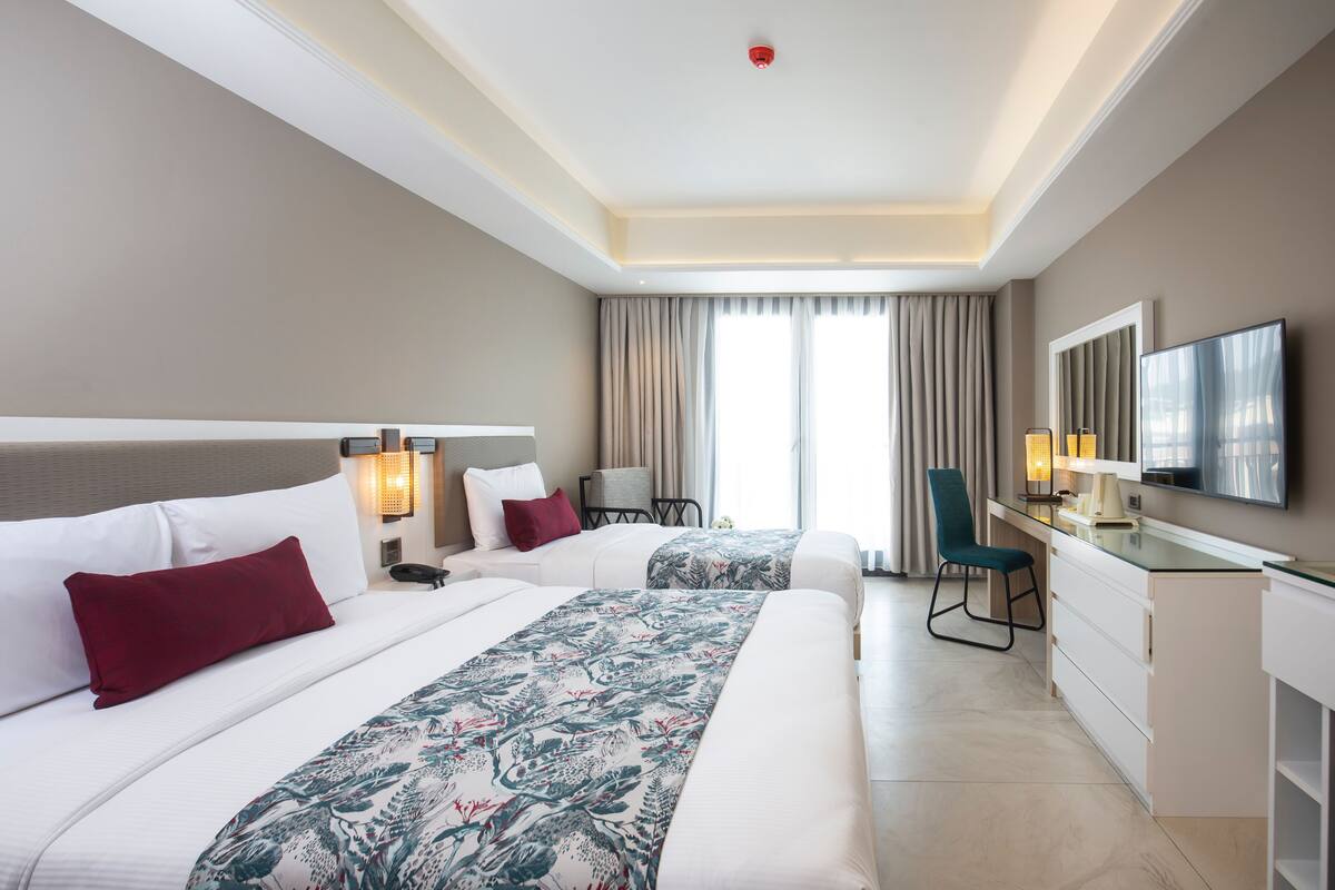 Une chambre d’hôtel avec deux lits, un bureau, une chaise, une télévision et une fenêtre avec des rideaux.
