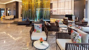 Un hall d’hôtel moderne avec un sol en marbre, des espaces de détente confortables et un grand mur décoratif.