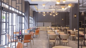 Un restaurant moderne avec de hauts plafonds, des luminaires suspendus et un mélange de chaises orange et beige.