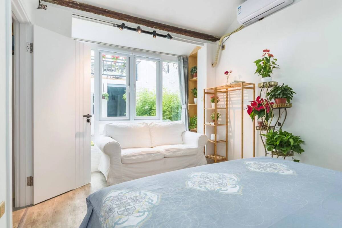 Um quarto com uma cama, um sofá branco, uma janela e uma estante com plantas.