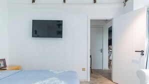 Un dormitorio con una cama, un televisor montado en la pared y una puerta que da a otra habitación.