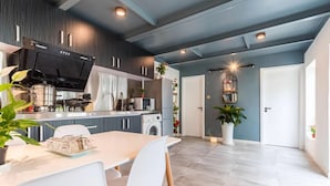 Cocina moderna con horno empotrado, microondas y lavadora. Cuenta con una zona de comedor con mesa y sillas.