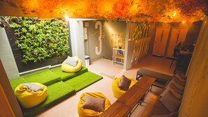 A modern lounge area with green artificial grass, yellow bean bag chairs, a wooden bench, and a wall with a large number '3'.