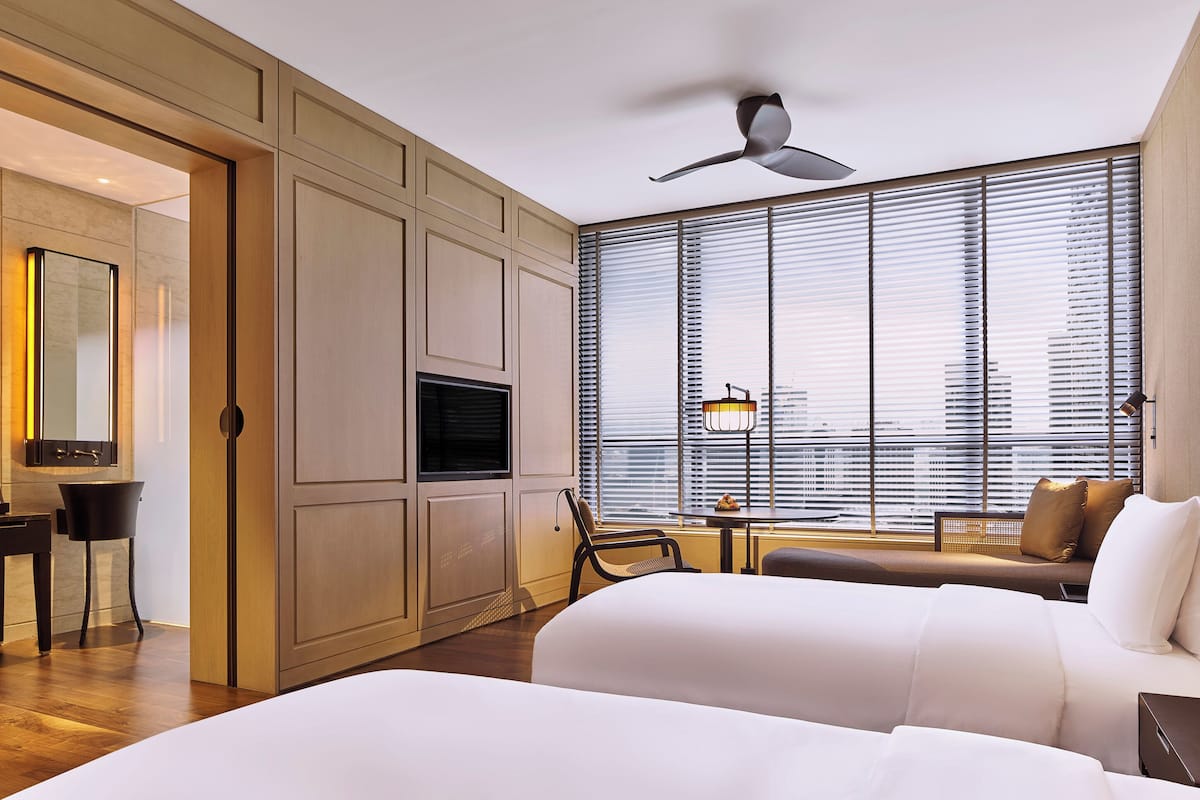Une chambre d’hôtel équipée d’un lit, d’un bureau, d’une chaise, d’une télévision et d’une fenêtre avec des stores.