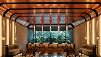 A modern lobby with a reflective floor, a seating area with sofas and chairs, and a large window with a view of greenery.
