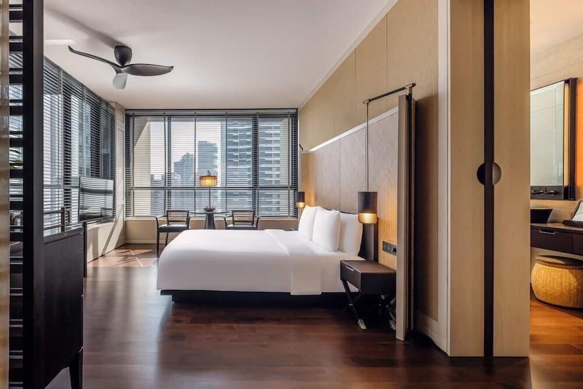 Une chambre d’hôtel moderne dotée d’un grand lit, d’un bureau, d’une chaise et offrant une vue sur la ville grâce à de grandes fenêtres.