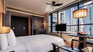 Une chambre d’hôtel moderne dotée d’un grand lit, d’une télévision, d’une table à manger et offrant une vue sur la ville grâce à de grandes fenêtres.