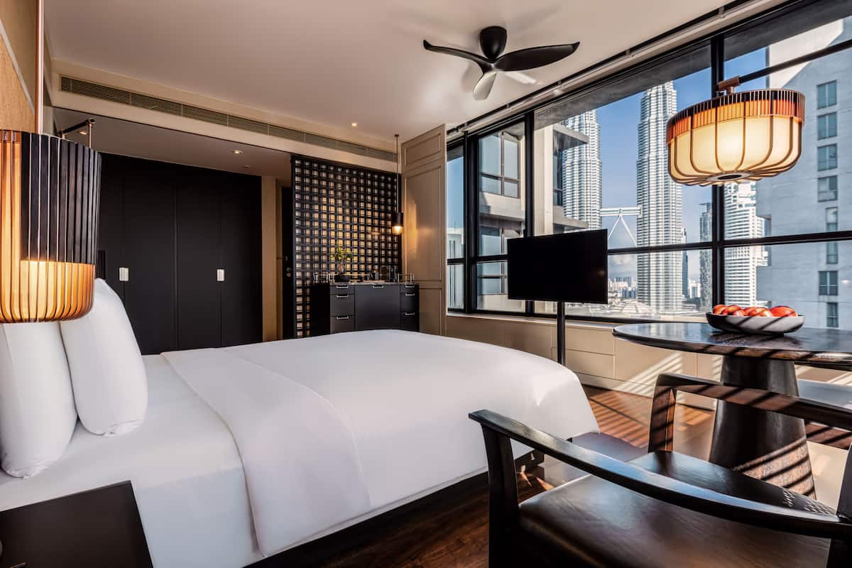 Une chambre d’hôtel moderne dotée d’un grand lit, d’une télévision, d’une table à manger et offrant une vue sur la ville grâce à de grandes fenêtres.