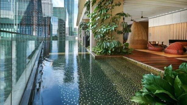 Un bâtiment moderne doté d’une façade en verre, d’un élément décoratif aquatique et offrant une vue sur les tours Petronas.