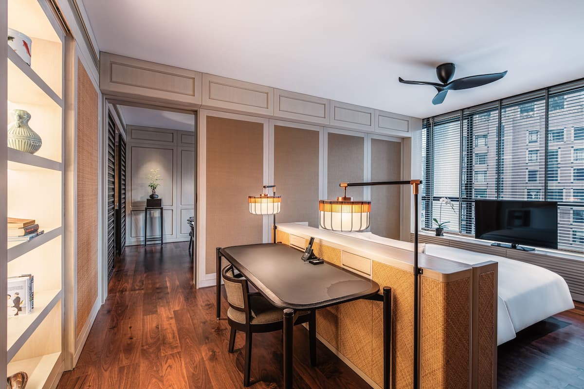 Une chambre d’hôtel avec un plancher en bois, une table à manger avec des chaises, un téléviseur, un lit et une fenêtre avec des stores.