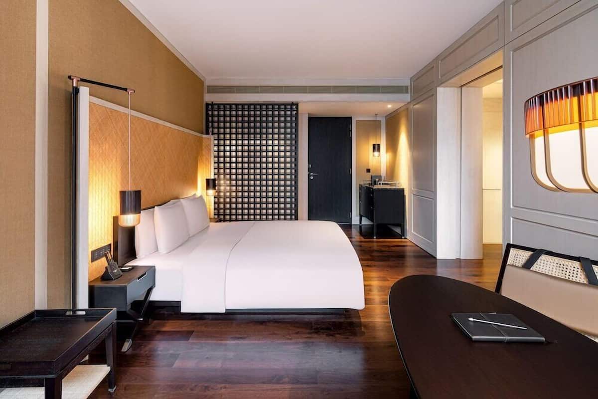 Une chambre d’hôtel moderne, dotée d’un grand lit, d’un bureau, d’une chaise, d’une petite table, d’une lampe, d’un mur décoratif et d’une porte donnant accès à une salle de bain.
