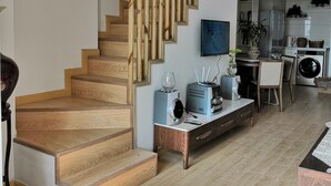 A modern living space with a wooden staircase, a dining area with a table and chairs, and a kitchen area with appliances. - Emma's home (Suzhou)