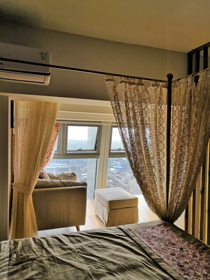 A bedroom with a bed, a window, and a view of the city.