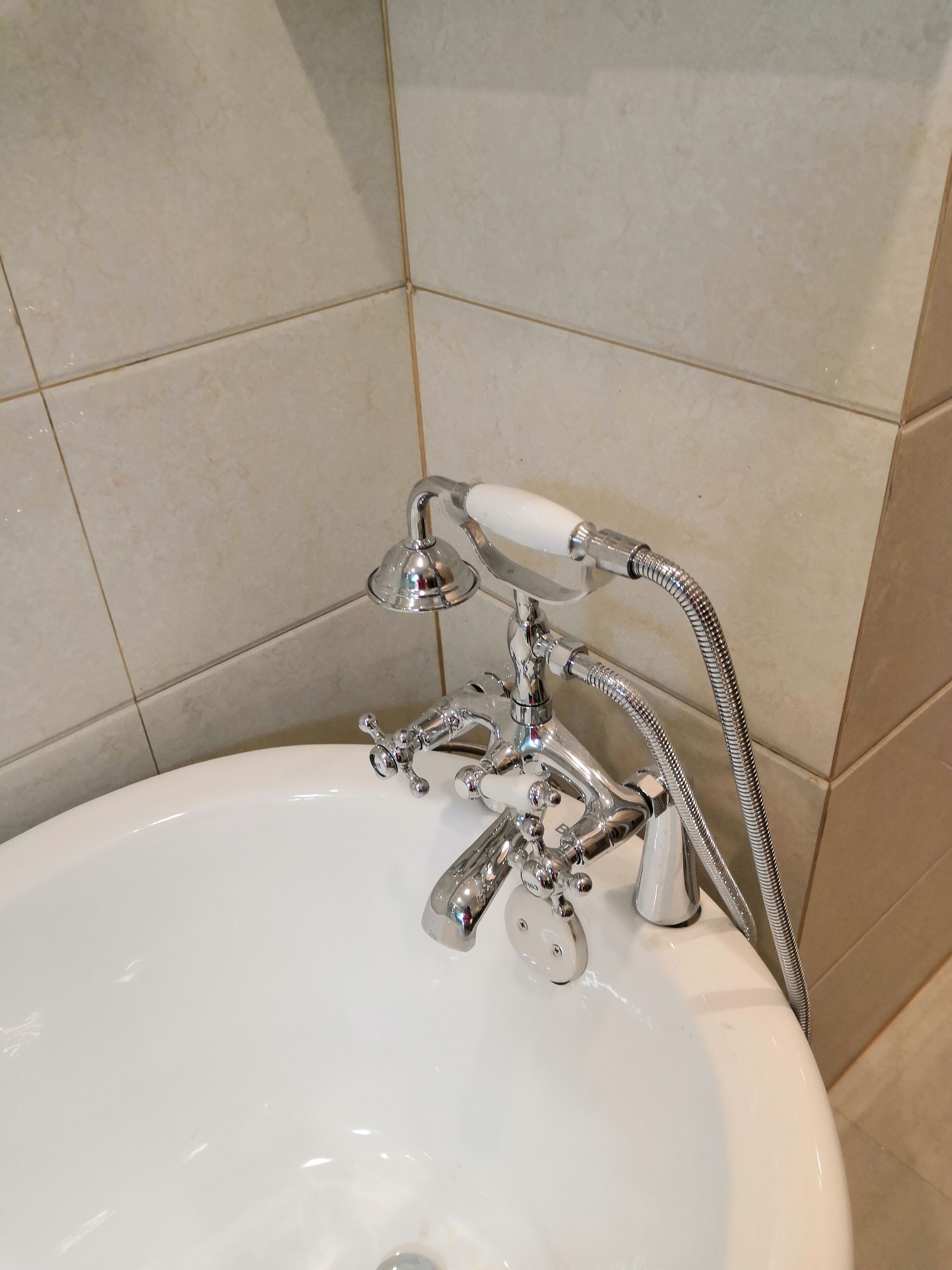 Un baño con lavamanos blanco, grifo cromado y ducha de mano.