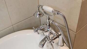 Un baño con lavamanos blanco, grifo cromado y ducha de mano.