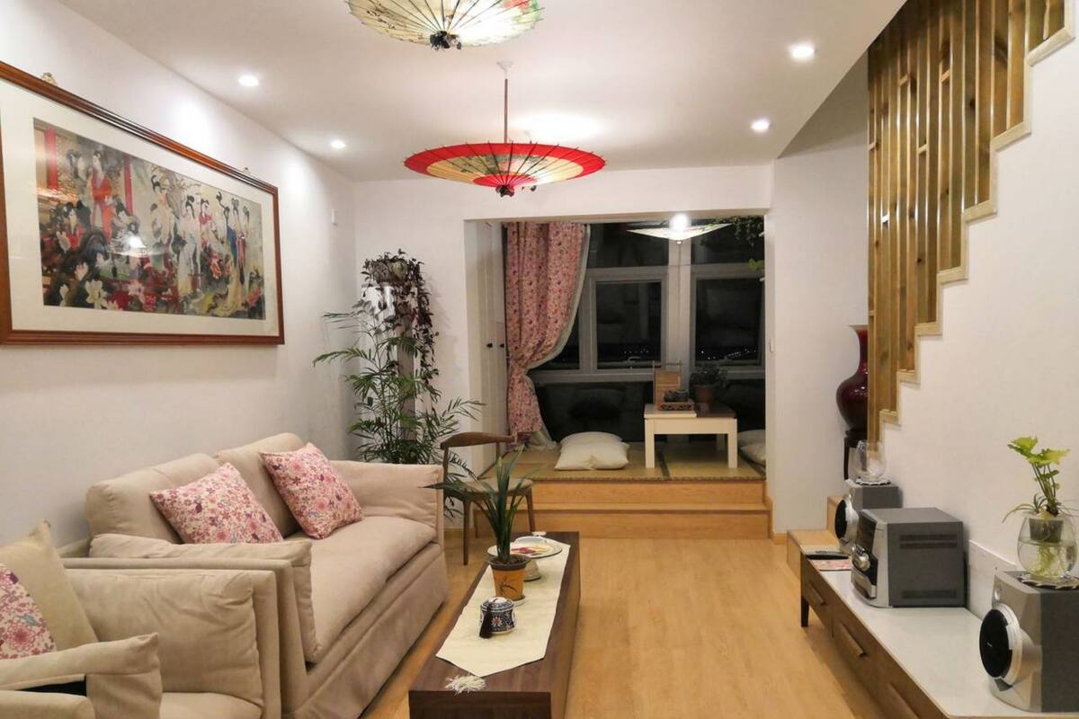 A living room with a beige sofa, a coffee table, a potted plant, and a painting on the wall.