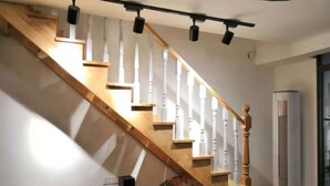 A staircase with wooden steps and white balusters, a wall-mounted air conditioner, and a wooden console table with a speaker. - Emma's home (Suzhou)