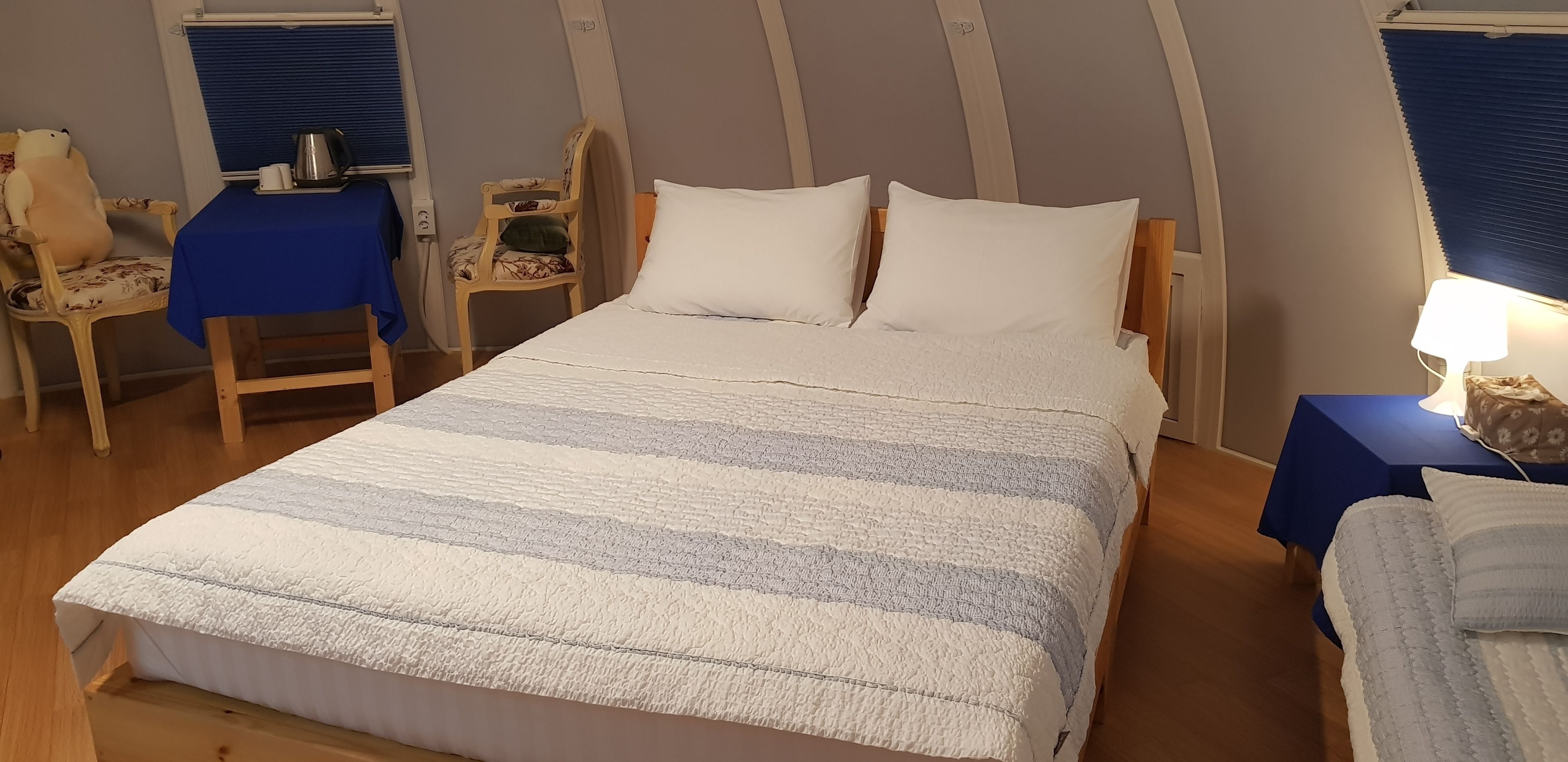 Un dormitorio con una cama, dos sillas, una mesa con un hervidor y una lámpara.