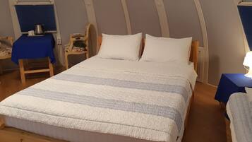 Un dormitorio con una cama, dos sillas, una mesa con un hervidor y una lámpara.