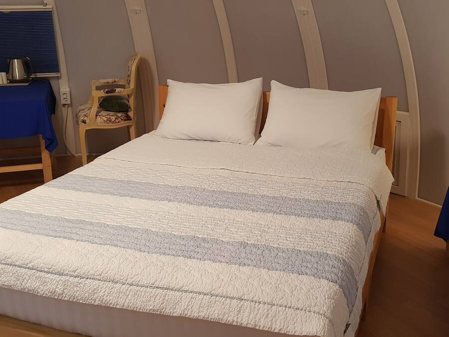 Un dormitorio con una cama, dos sillas, una mesa con un hervidor y una lámpara.