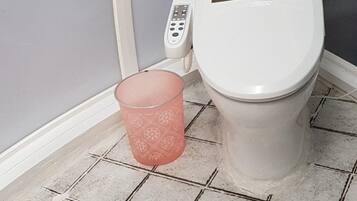 Un baño con inodoro, un bote de basura rosa y un desagüe en el piso.