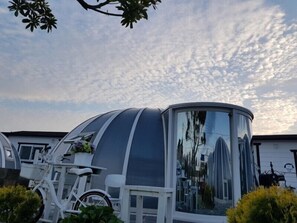 A modern, dome-shaped structure with a reflective surface, possibly a conservatory or greenhouse, adjacent to a white building with a visible window and a sign. - Jeju Igloo Pension (Jeju City)