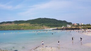 Una playa con agua cristalina, gente y una colina al fondo.