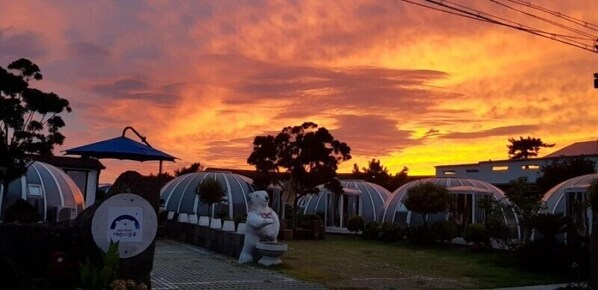A row of dome-shaped structures with a garden in the foreground and a sunset in the background. - Jeju Igloo Pension (Jeju City)