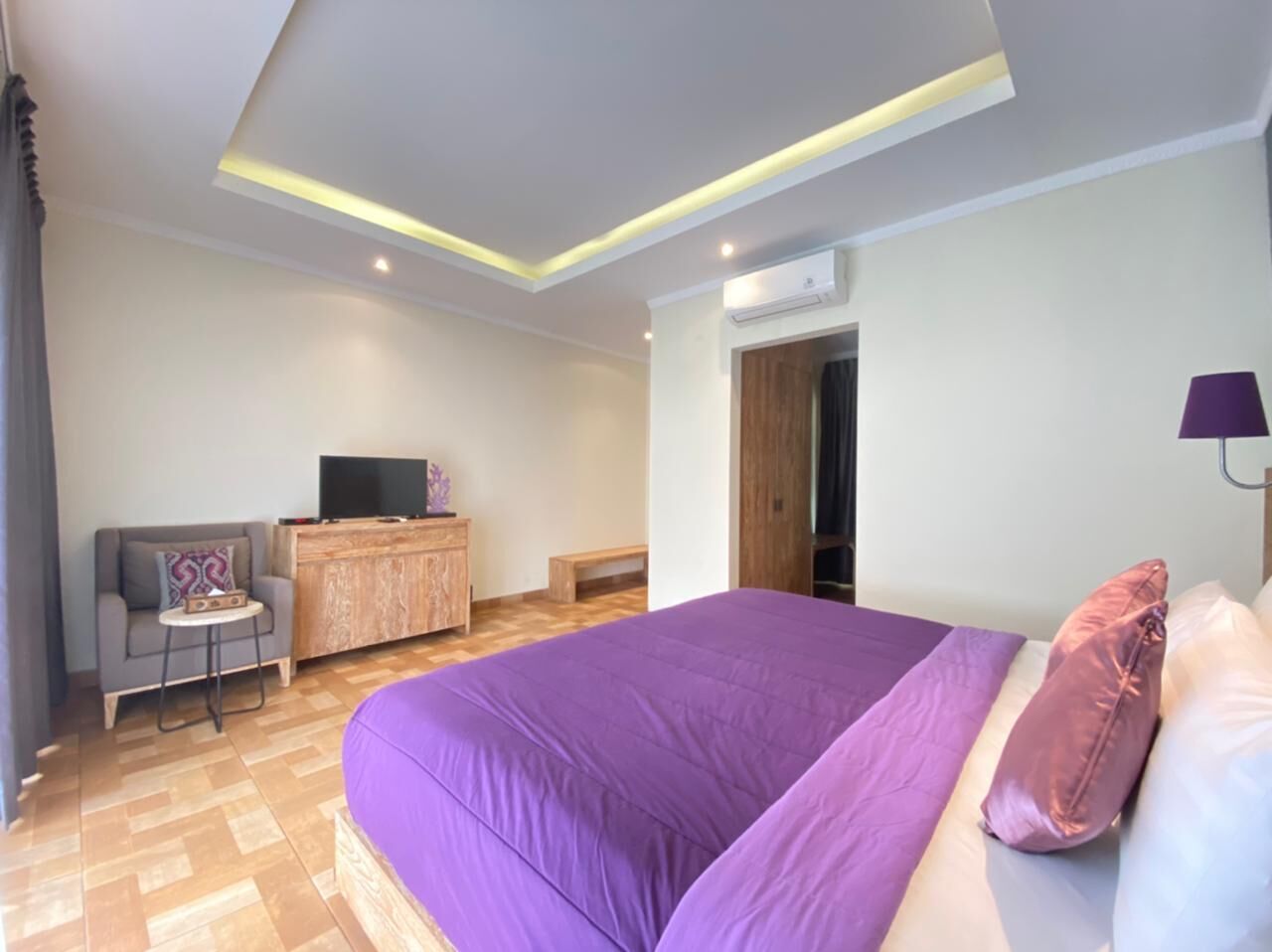 Una camera da letto moderna con un letto grande, un comò in legno, una televisione e un tavolino.