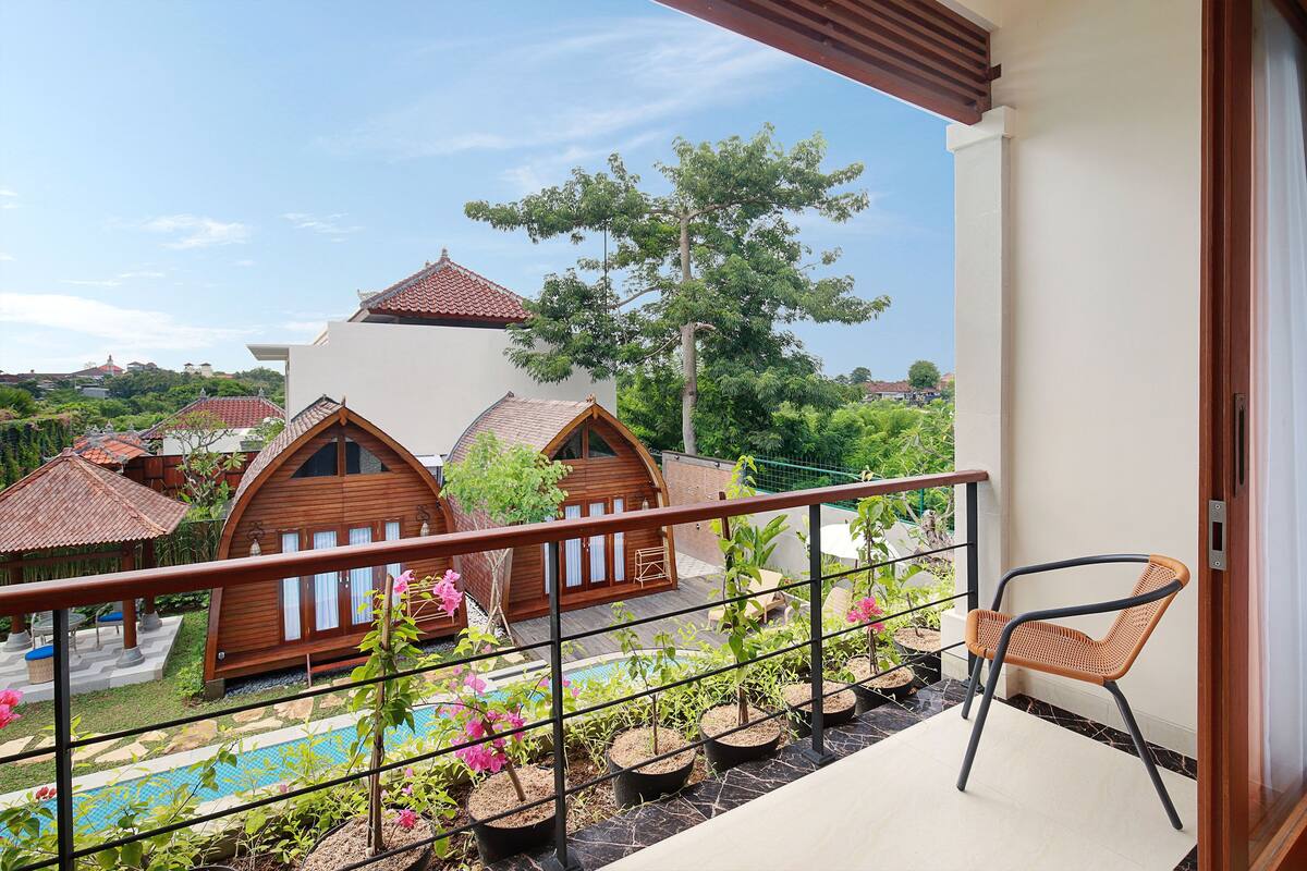 A balcony with a view of wooden cabins, a pool, and potted plants.
