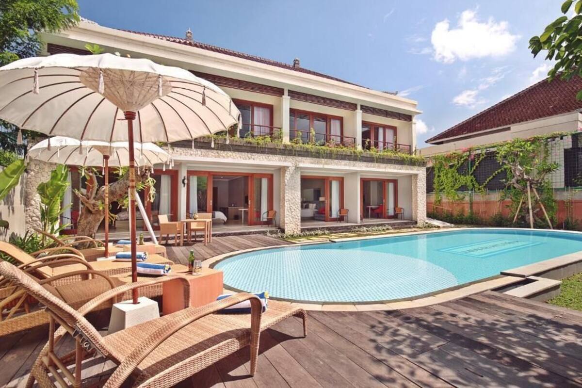 A two-story house with a swimming pool, outdoor furniture, and umbrellas.