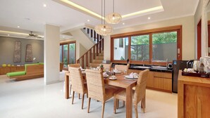 A modern kitchen with a dining area, wooden furniture, and large windows. - Kubu GWK Villa (Jimbaran)