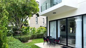 A modern house with a glass door leading to a patio with outdoor furniture.